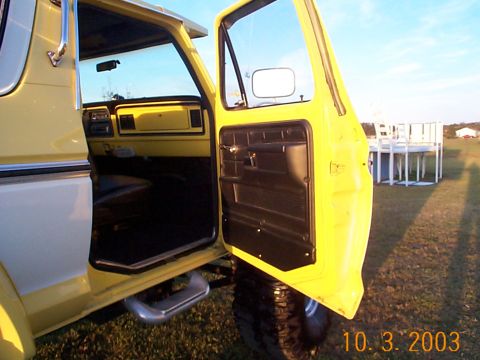1978 Ford Bronco - The interior of a 1978 Ford Bronco shows a yellow dashboard and black door panel with the driver's door ajar.