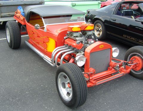 2007 Ford Mustang - A custom red hot rod with a powerful engine is parked alongside other vehicles.