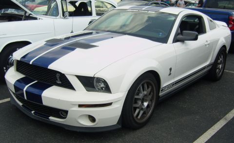 2007 Ford Mustang - A white 2007 Ford Mustang GT500 with racing stripes is parked at an outdoor event.
