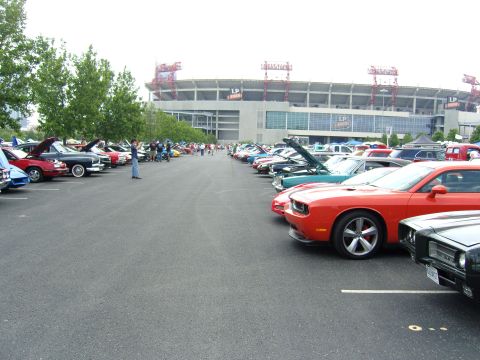 2007 Ford Mustang - An orange Dodge Challenger is parked in a lot full of cars, with a stadium visible in the distance.