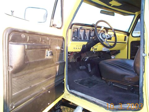 1978 Ford Bronco - The interior of a yellow truck is visible with the driver's side door open, revealing the dashboard and seating area.