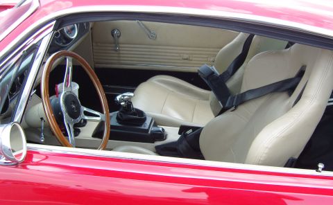 2007 Ford Mustang - The interior of a red 1967 Mustang features tan racing seats, a wooden steering wheel, and a manual shifter.