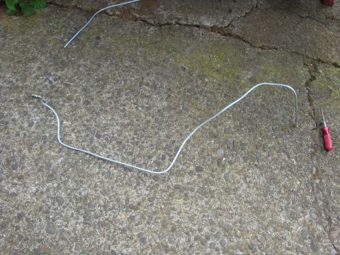 1989 Ford Bronco - A detached metal brake line lies on a concrete surface next to a red-handled screwdriver.