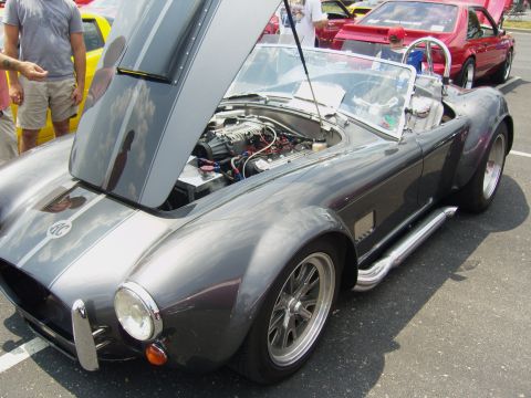 2007 Ford Mustang - A dark gray convertible sports car with racing stripes is parked outdoors, with its hood open to display the engine.