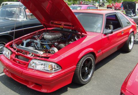 2007 Ford Mustang - Red Ford Mustang coupe with hood open, revealing the engine bay. Seen at an outdoor car event.