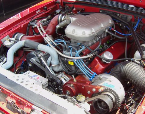 2007 Ford Mustang - Close-up of a modified engine bay a prominent supercharger and custom red components.