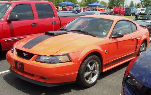 2007 Ford Mustang - Orange 2007 Ford Mustang coupe with black racing stripes on hood and side.