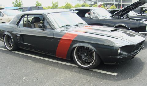 2007 Ford Mustang - A modified classic car with a distinctive red stripe and aggressive stance is parked at an event.