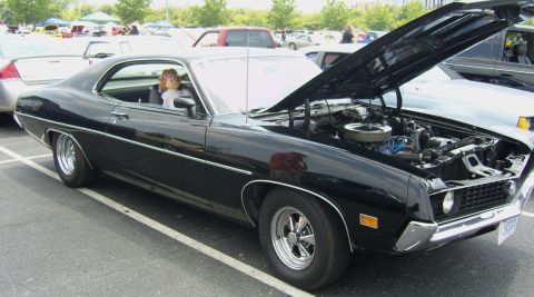 2007 Ford Mustang - A black classic coupe is parked with its hood open, revealing the engine bay. A child sits in the driver's seat.