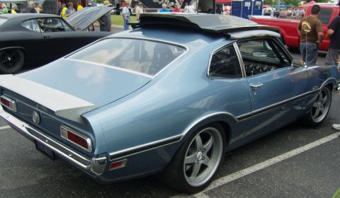 2007 Ford Mustang - A classic blue coupe with a spoiler and custom wheels is parked at an outdoor event.
