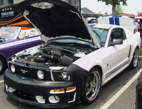 2007 Ford Mustang - A white Ford Mustang with its hood open is parked next to a purple car at an outdoor event.