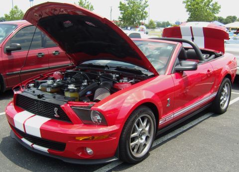 2007 Ford Mustang - Red 2007 Ford Mustang convertible with racing stripes and hood open at an outdoor event.