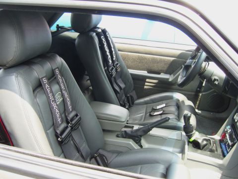 2007 Ford Mustang - The interior of a car shows gray leather racing seats equipped with Safecraft harnesses and a manual transmission shifter.