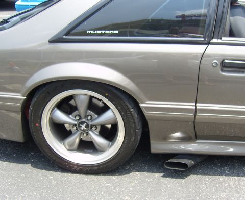 2007 Ford Mustang - Side profile of a grey 1987 Ford Mustang, showing the rear wheel and exhaust pipe.