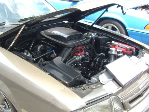 2007 Ford Mustang - Customized engine bay in a tan car, with another vehicle visible behind it.