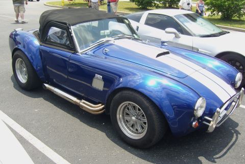 2007 Ford Mustang - A blue convertible with white racing stripes and side exhaust pipes is parked next to another vehicle.