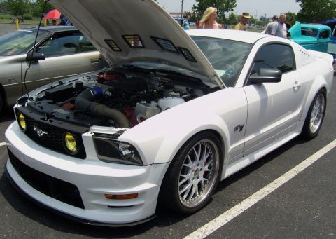 2007 Ford Mustang - A white Ford Mustang GT is parked with its hood open, revealing the engine and custom wheels.
