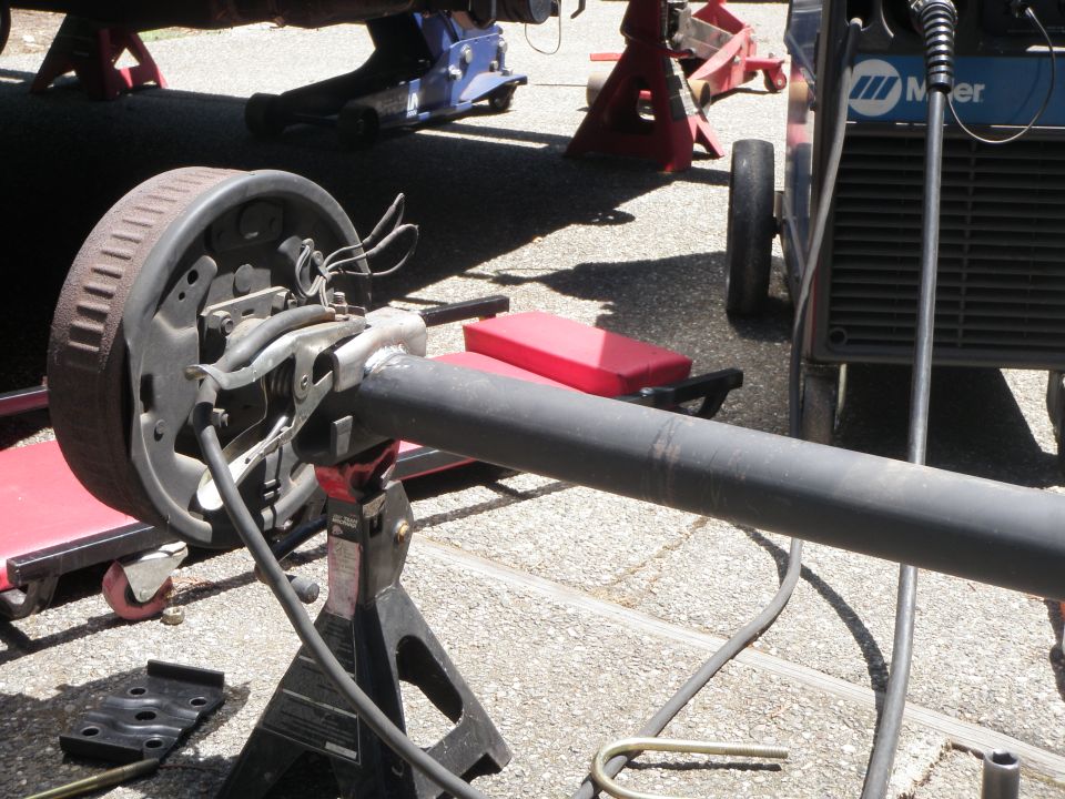 Rear axle assembly with drum brake, supported by jack stands, with welding equipment nearby