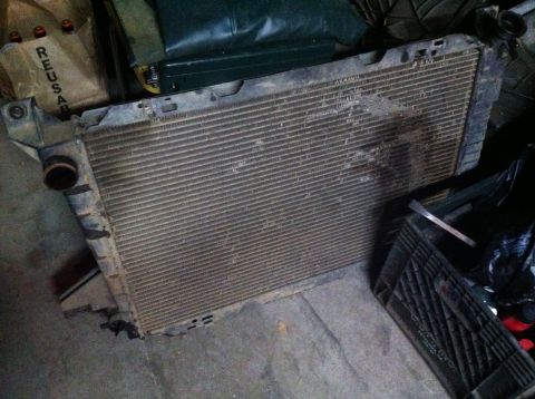 1989 Ford Bronco - A vehicle radiator sits on a concrete floor, surrounded by storage bins and bags.