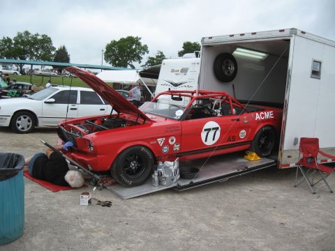 1968 Shelby GT500 - A red race car, possibly a modified Ford Mustang, is being serviced next to a trailer. Another car is parked nearby.
