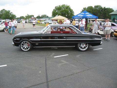 1968 Shelby GT500 - Side view of a black 1964 Ford Falcon coupe parked outdoors with people and tents in the background.