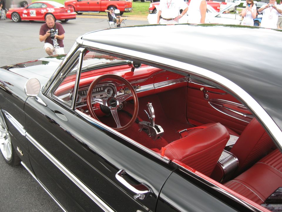 Black coupe interior with red seats, wood steering wheel, and floor shifter, viewed from the passenger side