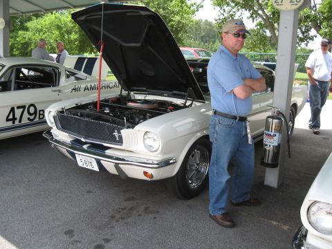 1968 Shelby GT500 - A man stands next to a classic Ford Mustang at an outdoor event, with another similar car visible.