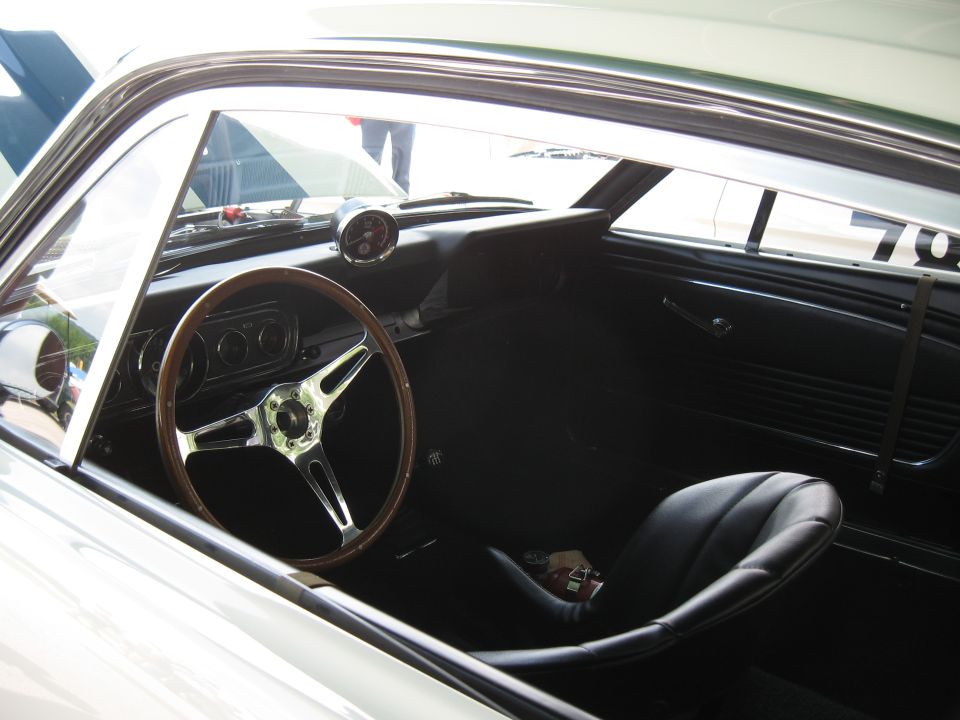 Interior view of a 1965 Mustang with wood steering wheel and racing seat. Number 70 visible