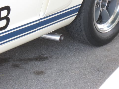 1968 Shelby GT500 - A portion of a classic car is visible, blue racing stripes along the side and a chrome exhaust pipe.