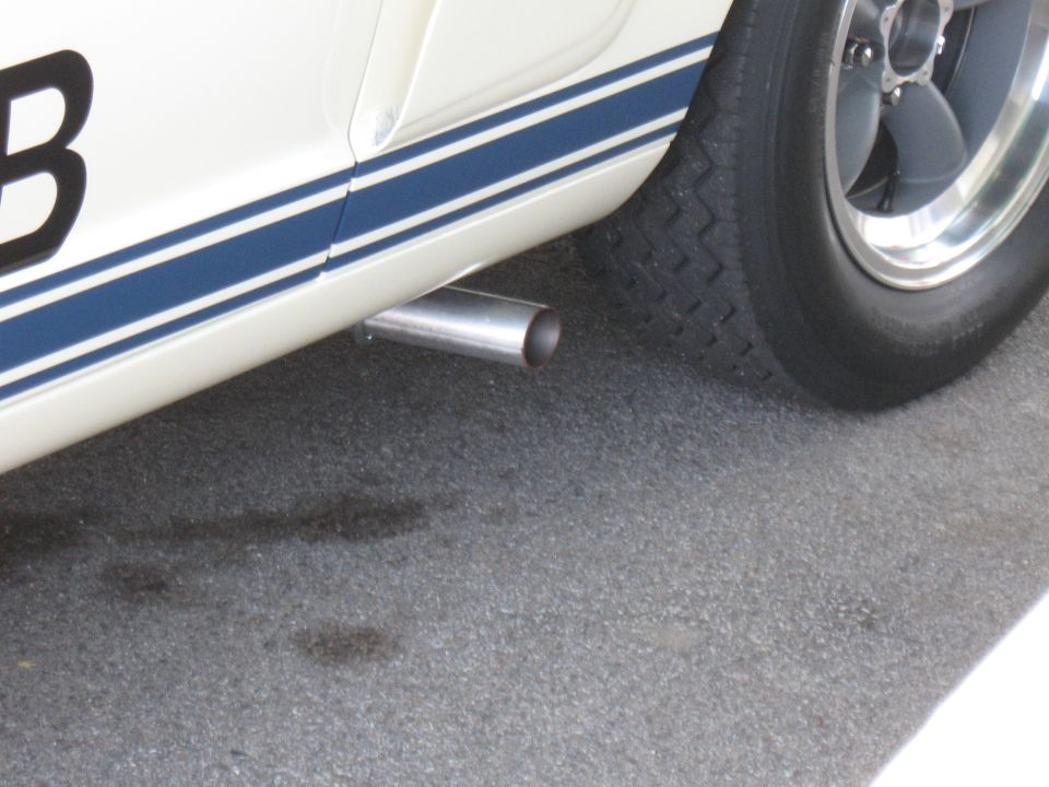 Close-up of a white car with blue stripes, showing the exhaust pipe and a wheel