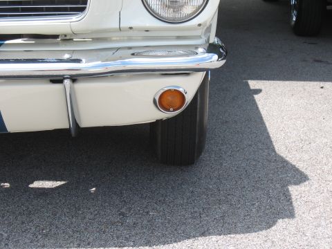 1968 Shelby GT500 - Close-up of the front corner of a white 1967 Ford Mustang, showing the chrome bumper and an orange turn signal light.