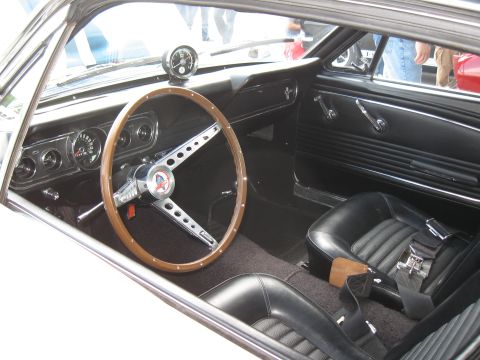 1968 Shelby GT500 - The interior of a classic Ford Mustang shows a wood-rimmed steering wheel and black vinyl seats.