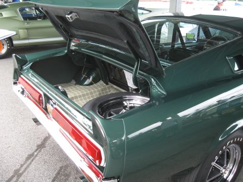 1968 Shelby GT500 - The trunk of a 1968 Shelby GT500 is open, revealing a spare tire and plaid lining, with another similar car in the background.