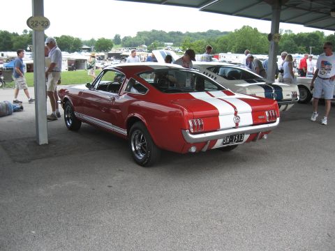 1968 Shelby GT500 - Red 1966 Shelby GT350 Mustang with white stripes, another Shelby behind it at an outdoor event.
