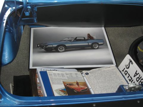 1968 Shelby GT500 - A photograph of a 1969 Ford Mustang convertible is displayed within the trunk of a blue vehicle, alongside other documents.
