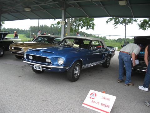 1968 Shelby GT500 - A blue 1968 Shelby GT500 convertible is displayed at a car show, with other vehicles and attendees visible.
