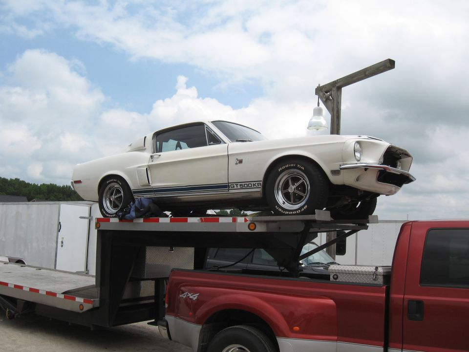White 1968 Shelby GT500KR coupe on a car hauler, side view with blue stripe and GT500KR badging