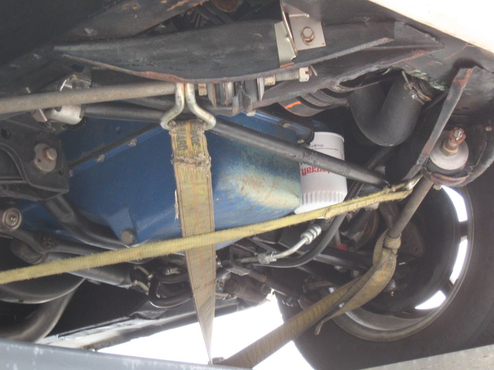 Underside view of a vehicle with a blue oil pan, oil filter, and yellow tie-down straps