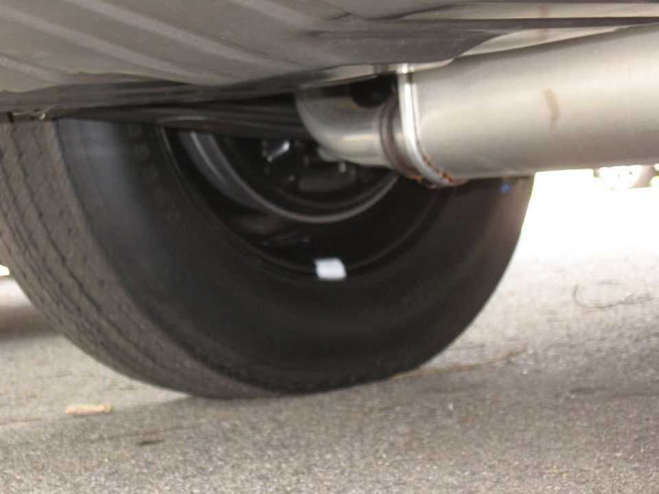 Close-up of a car's exhaust pipe and rear tire from underneath