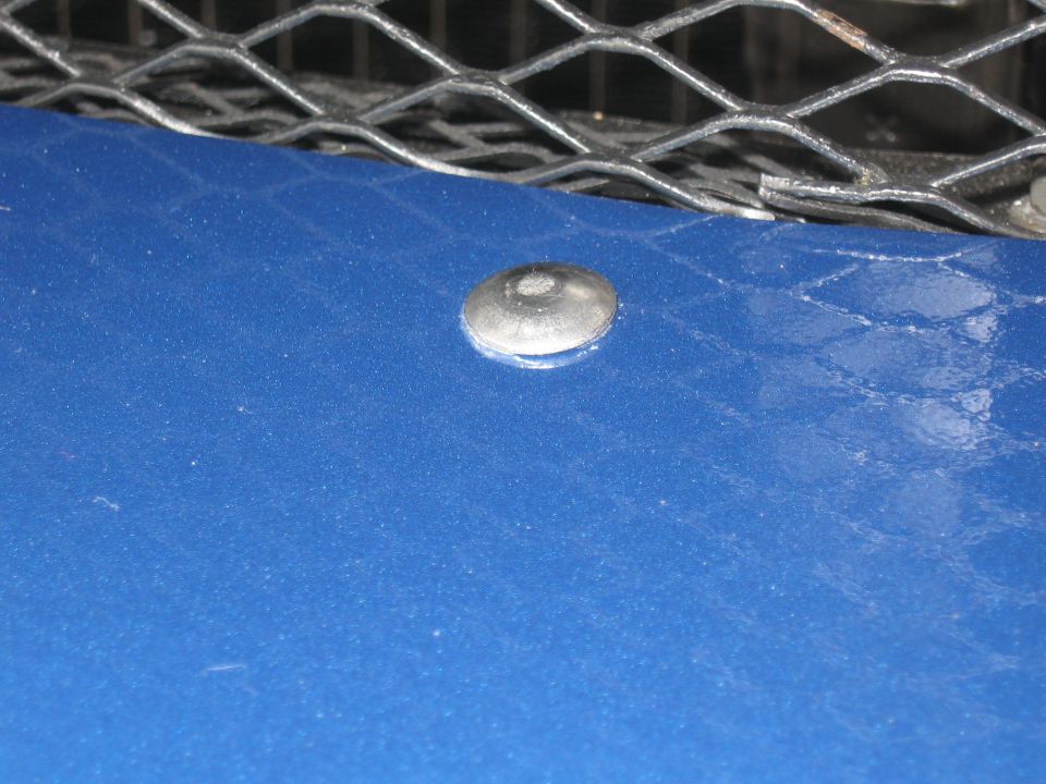 Blue car hood with a silver rivet and a diamond-patterned metal grille above