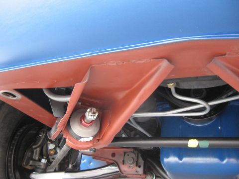 1968 Shelby GT500 - A close-up view of the undercarriage of a blue vehicle, revealing suspension parts and red protective coating. The Supermotors.net logo is…
