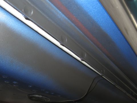 1968 Shelby GT500 - Close-up of a car's blue door edge and black trim, showing rivets and a red stripe detail.