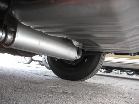 1968 Shelby GT500 - Close-up of a vehicle's exhaust system, showing the muffler and part of the tire. Another vehicle is visible in the background.