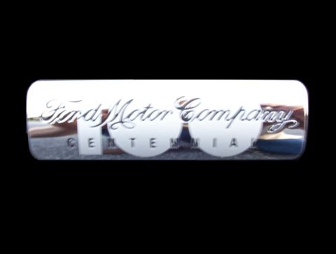 2003 Ford Taurus - Close-up of a chrome 'Ford Motor Company 100 Centennial' emblem mounted on a black body panel, with the script lettering and large 100 in r…