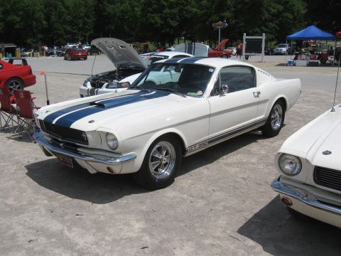 1968 Shelby GT500 - A white 1965 Shelby GT350 with blue racing stripes is parked outdoors at an event. Another car is visible to the right.
