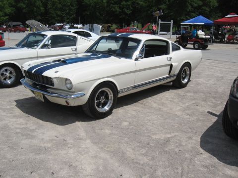 1968 Shelby GT500 - A white 1967 Shelby GT350 with blue racing stripes is parked at an outdoor event, with another classic Mustang visible behind it.
