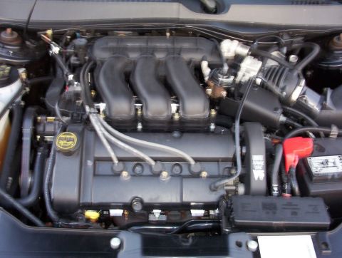2003 Ford Taurus - Engine bay of a transverse V6 sedan, showing the black ribbed composite intake manifold, front valve cover with plug wires running to the c…
