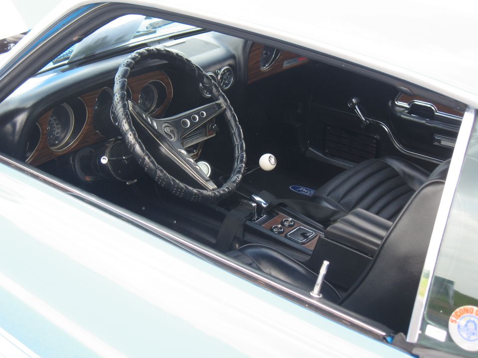Interior of a 1969 Ford Mustang with woodgrain trim, black seats, and a white shift knob