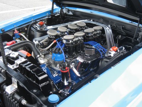 1968 Shelby GT500 - The engine bay of a light blue classic car features a V8 engine with multiple carburetors and chrome accents.