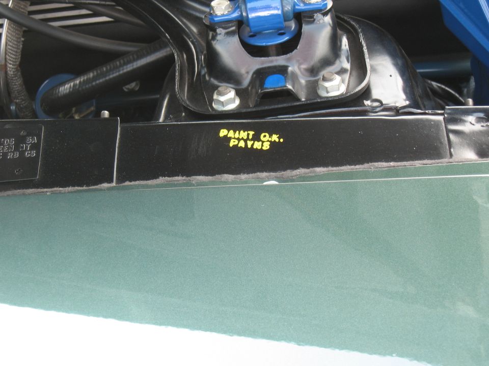 Close-up of car engine bay showing yellow text 'PAINT O.K. PAYNE' on a black bracket
